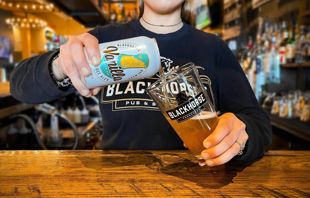 A person pouring beer out of a can to a Blackhorse branded glass.